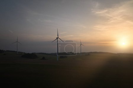 Foto de Vista aérea y panorámica de la silueta de la central eólica contra la puesta del sol. Inspección aérea con drones de tres generadores eléctricos eólicos. - Imagen libre de derechos