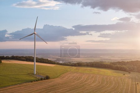 Téléchargez les photos : Aerial view of wind  power plant in agricultural landscape, illuminated by setting sun light. - en image libre de droit