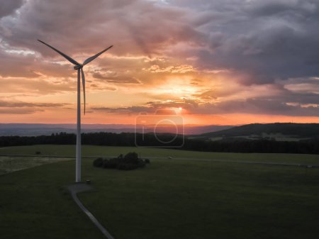 Photo for Aerial view of wind  power plant in full load, illuminated with dramatic light, green landscape against sunset sky with clouds. Aerial, drone inspection of wind turbine. - Royalty Free Image