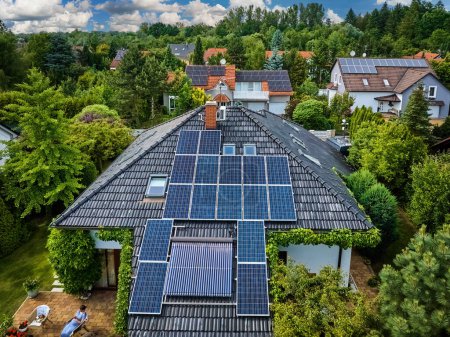 Photo for Aerial view of the roofs of houses covered with solar panels. Family houses in gardens, photovoltaic panels on the roof, summer, blue sky with white clouds. Home Electricity Generation, green living. - Royalty Free Image