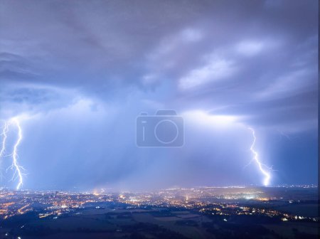 Photo for Spectacular, aerial shot of a city hit by multiple lightning. Dramatic, real drone shot of a massive storm over city. Lightning between the clouds and the ground. Blue and purple colors. - Royalty Free Image