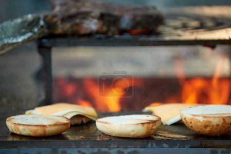 Photo for A chef prepares burgers on an outdoor grill. Close up of cooking at garden festival, flames, shallow depth of field, very colorful blurred background, evening at garden festival. - Royalty Free Image