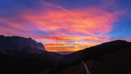 Téléchargez les photos : Coucher de soleil rouge sur Passo delle Erbe avec fond de sommets de Dolomite. Ciel coloré avec des nuances de rouge, orange et bleu, vue aérienne de haute altitude. - en image libre de droit
