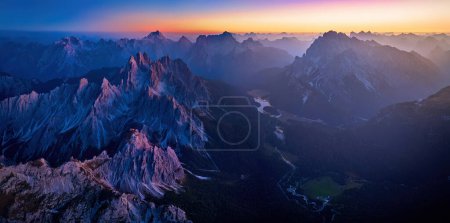 Foto de Panorama vespertino de los Dolomitas desde gran altura. Sombras azul-púrpura en los valles, picos rojizos de los rocosos tres mil, cielo amarillo-naranja. Fabuloso paisaje de montaña. - Imagen libre de derechos