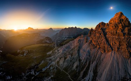 Téléchargez les photos : Le massif orange de Tre Cime et la vue sur le panorama des Dolomites avec le soleil couchant et la pleine lune contre le ciel nocturne bleu foncé. Automne en randonnée dans les Dolomites, Italie. - en image libre de droit
