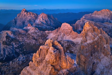Téléchargez les photos : Vue en haute altitude du massif rocheux de Tre Cime, Dolomites, Italie. Vue aérienne des sommets de montagne de couleur dorée contre le ciel bleu foncé et la vallée. Crépuscule dans les Dolomites, atmosphère extrêmement colorée. - en image libre de droit
