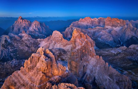 Téléchargez les photos : Vue panoramique du massif rocheux de Tre Cime d'en haut, Dolomites, Italie. Vue aérienne des sommets de montagne dorés contre le ciel bleu foncé et la vallée, atmosphère colorée. - en image libre de droit