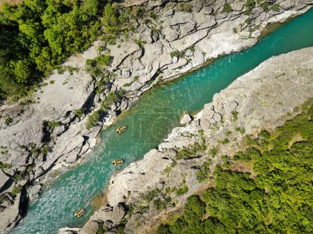 Photo for White water rafting.  Adventure and sport. A yellow raft floating among the rocks on the crystal clear, blue-green water. Perpendicular drone view of the rafters floating on Vjose river, Albania. - Royalty Free Image