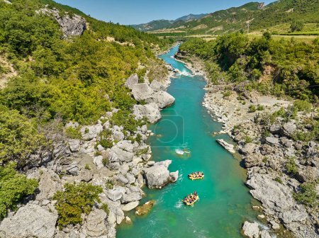 Wildwasserrafting. Abenteuer und Sport. Ein gelbes Floß, das zwischen den Felsen auf dem kristallklaren, blaugrünen Wasser schwimmt. Senkrechte Drohnenaufnahme der auf dem Fluss Vjose treibenden Flößer, Albanien.