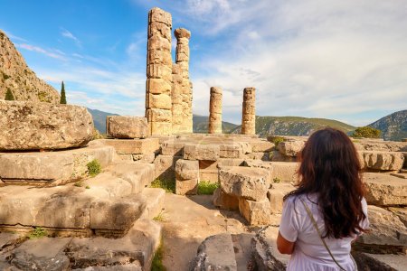 Photo for A long-haired woman from behind looking at  Apollo Temple or Apollonion and its doric pillars in sunset. Tourist spot, famous for oracle at the Apollo sanctuary. Mount Parnassus, Delphi, Greece. - Royalty Free Image
