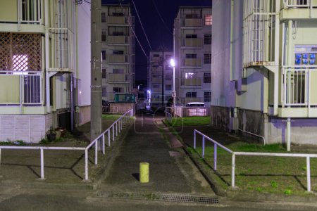 Téléchargez les photos : Passerelle sombre à travers des immeubles d'appartements de plusieurs étages la nuit. Photo de haute qualité - en image libre de droit