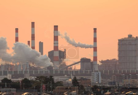 El humo sube de la planta industrial con el resplandor anaranjado del atardecer en cielo. Foto de alta calidad