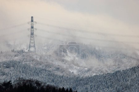 High voltage electrical transmission tower and wires over snowy mountain landscape. High quality photo