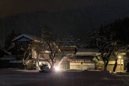 Téléchargez les photos : Plow pousse de la neige pendant la tempête sur une grande maison japonaise la nuit. Photo de haute qualité - en image libre de droit