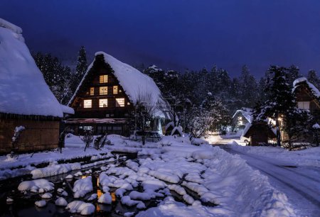 Foto de Snow covered Japanese farmhouse in historic village by woods at night . High quality photo - Imagen libre de derechos