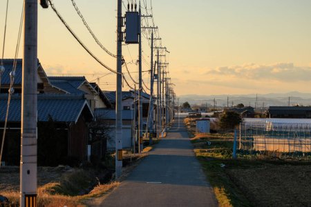 Enge Landstraße durch Häuser und Strommasten bei Sonnenuntergang. Hochwertiges Foto
