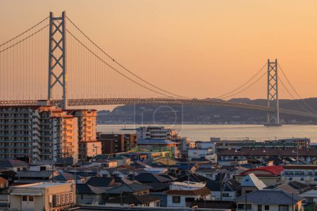 Photo for Orange sunset glow in sky over suspension bridge and dense small town. High quality photo - Royalty Free Image