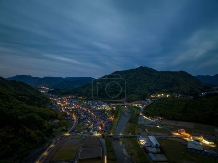 Téléchargez les photos : Vue aérienne des lumières de la petite ville rurale entre les montagnes au crépuscule. Photo de haute qualité - en image libre de droit