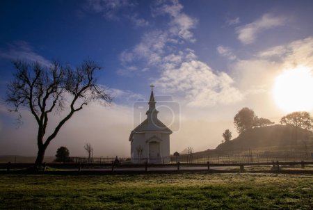 Early morning sun, mist, and fog on small rural church in field. High quality photo