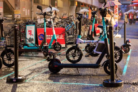 Foto de Osaka, Japón - 29 de abril de 2023: Lluvia fuerte en mini bicicletas eléctricas compartidas y scooters estacionados en la calle de la ciudad. Foto de alta calidad - Imagen libre de derechos