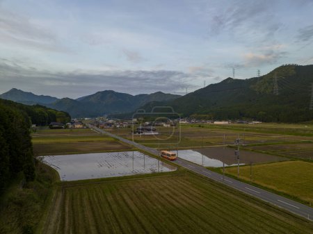 Téléchargez les photos : Bus sur la route ouverte à travers les rizières inondées dans les montagnes rurales du Japon au crépuscule. Photo de haute qualité - en image libre de droit