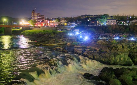 Foto de Las linternas iluminan la orilla del río junto a una pequeña cascada en la ciudad por la noche. Foto de alta calidad - Imagen libre de derechos