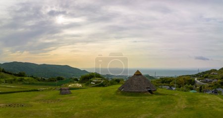 Photo for Historic Jomon huts on grassy hillside over coastal Japan landscape. High quality photo - Royalty Free Image