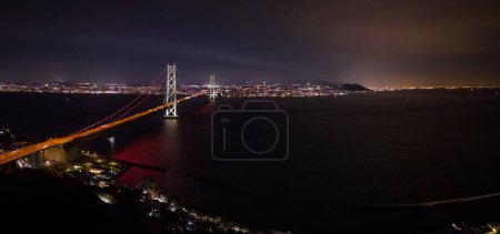 Photo for Panoramic night view of suspension bridge connecting city lights over dark water. High quality photo - Royalty Free Image