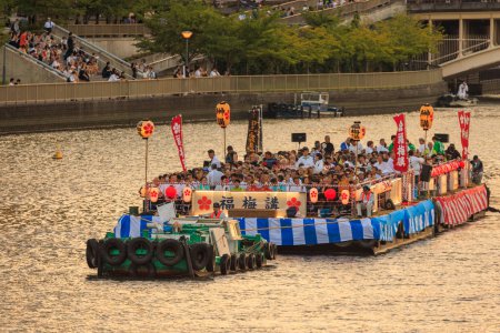 Photo for Osaka, Japan - July 25, 2023: Tug boat pulls crowded barge down river at summer festival. High quality photo - Royalty Free Image