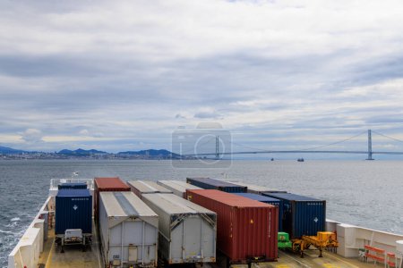 Photo for Kobe, Japan - September 23, 2023: Shipping containers on ferry sail by Akashi suspension bridge. High quality photo - Royalty Free Image