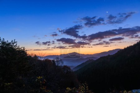 Téléchargez les photos : Brouillard aube et brume dans la vallée de montagne avec lueur du lever du soleil et la lune dans le ciel. Photo de haute qualité - en image libre de droit