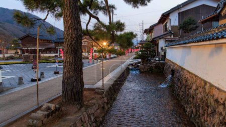 Téléchargez les photos : Flux d'eau dans le canal par la rue historique dans la ville de Takeda, Japon au crépuscule. Photo de haute qualité - en image libre de droit