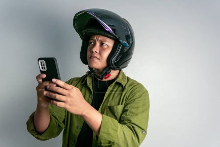 Foto de Adulto asiático hombre confuso cuando se mira a su teléfono mientras usa casco de motocicleta - Imagen libre de derechos