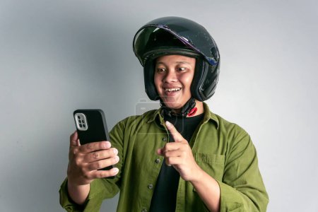Foto de Hombre asiático adulto sonriendo cuando mira a su teléfono mientras usa casco de motocicleta - Imagen libre de derechos