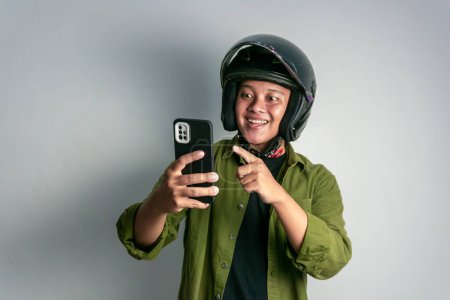 Foto de Hombre asiático adulto sonriendo cuando mira a su teléfono mientras usa casco de motocicleta - Imagen libre de derechos