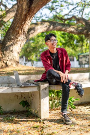 Photo for Young Asian man sitting outdoor with happy expression. A male college student smiling at the public park - Royalty Free Image