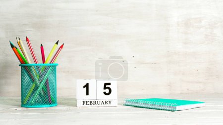 15. Februar. Das Konzept des Saisontermins. Bleistifte in einem Korb vor dem Hintergrund eines Notizbuchs und dem Datum des Monats. Leerraum-Kalenderwürfel kopieren.