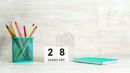 February 28 calendar. The concept of the date of the season. Pencils in a basket against the background of a notebook and the date of the month. Copy space calendar cube.