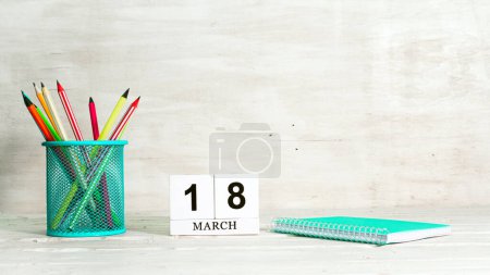 Téléchargez les photos : Calendrier du 18 mars. Le concept de la date de la saison. Crayons dans un panier sur fond de carnet et la date du mois. Copier espace calendrier cube - en image libre de droit
