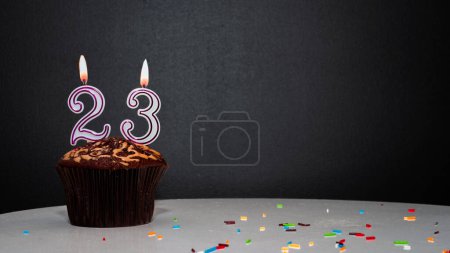 Téléchargez les photos : Muffin noir avec un numéro d'une bougie numéro 23. Copiez l'espace, une tarte sur fond noir, une carte pour féliciter votre anniversaire, anniversaire - en image libre de droit