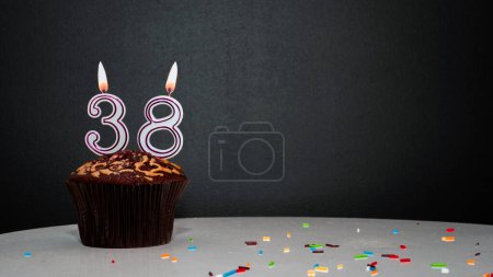 Foto de Muffin en negro con un número de una vela número 38. Copiar espacio, un pastel sobre un fondo negro, una tarjeta para felicitaciones en su cumpleaños, aniversario - Imagen libre de derechos