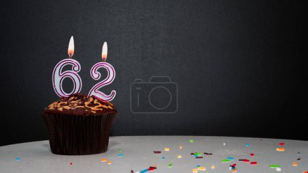 Téléchargez les photos : Muffin noir avec un numéro d'une bougie numéro 62. Copiez l'espace, une tarte sur fond noir, une carte pour féliciter votre anniversaire, anniversaire - en image libre de droit