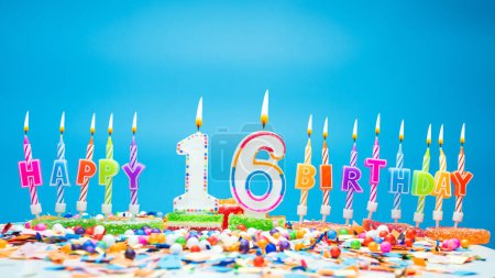 Téléchargez les photos : Happy birthday candle letters with the number sixteen on a beautiful blue background. Copy space Happy birthday greetings for 16 years old child, lit candles with holiday decorations - en image libre de droit