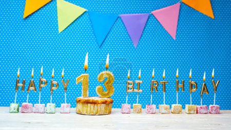 Photo for Happy birthday from the letters of candles number 13 on a blue background with polka dots white copy space. Happy birthday muffin with a burning golden candle for a thirteen year old child. - Royalty Free Image