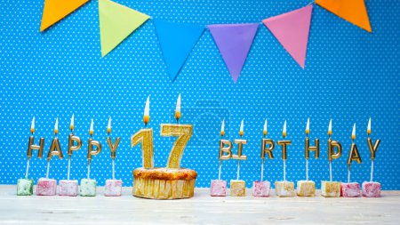 Photo for Congratulations on your birthday from the letters of candles number 17 on a blue background with polka dots white copy space. Happy birthday muffin with a burning golden candle for a seventeen year old. - Royalty Free Image