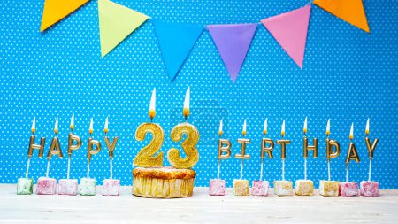 Téléchargez les photos : Congratulations on your birthday from the letters of candles number 23 on a blue background with polka dots white copy space. Happy birthday muffin with burning golden candle for twenty three. - en image libre de droit