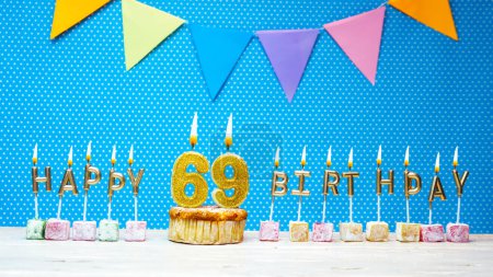 Foto de Happy birthday from number 69 candle letters on a blue background with white polka dot copy space. Happy birthday cupcake with burning golden candle for sixty nine years old. - Imagen libre de derechos