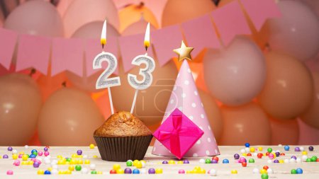 Téléchargez les photos : Decorations with balloons and a happy birthday candle with the number 23. Happy birthday greetings in pink flowers for twenty-three years for a girl, copy space. Muffin with a burning candle - en image libre de droit
