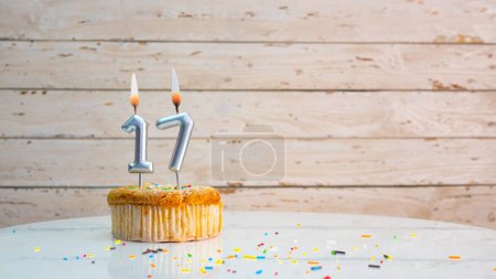 Photo for Happy birthday greetings for 17 years old from silver numbers against the background of white planks of mine space. Beautiful birthday card with a muffin with a burning candle for seventeen years - Royalty Free Image