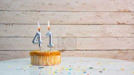 Foto de Happy birthday greetings for 41 years old from silver numbers against the background of white planks of mine space. Beautiful birthday card with a muffin with a burning candle for forty-one years. - Imagen libre de derechos